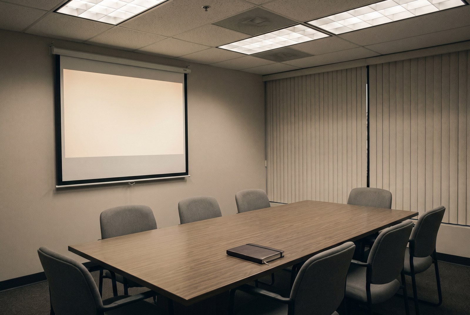 An empty meeting room with a blank rectangle of projector light on the wall and one closed notebook.